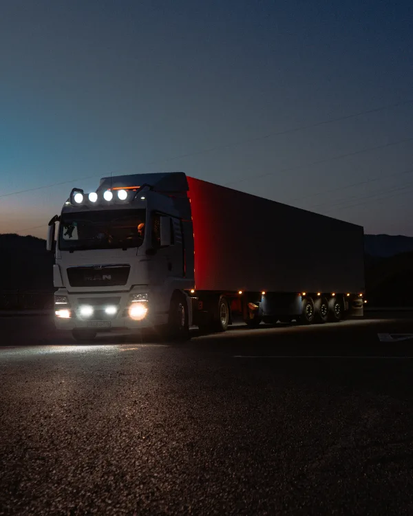 Cargo truck driving on a highway at night with illuminated road and city lights in the distance